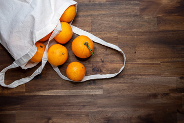 fresh unpeeled oranges placed in reusable nature textile bag on brown table.