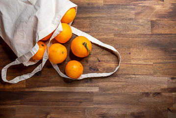fresh unpeeled oranges placed in reusable nature textile bag on brown table.