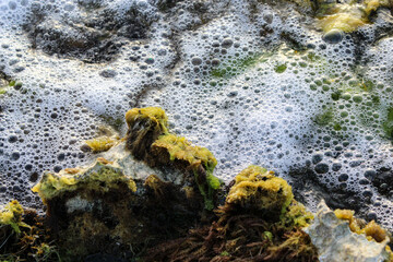 sea foam bubbles and water rolling up from the Caribbean sea over intercoastal rocks in the Aruban tide. gently flowing water peaceful tropical scene background.