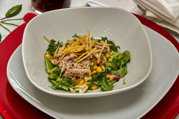 Fresh salad with tuna, corn, and crispy potatoes on a white plate.