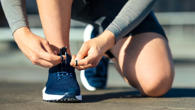 Morning running. Young man tying shoelaces on sneakers, on track, on street, panorama, free space, cropped