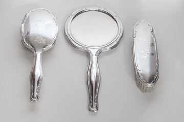 An antique hand mirror featuring a ornate silver handle and a round reflective surface. The mirror...