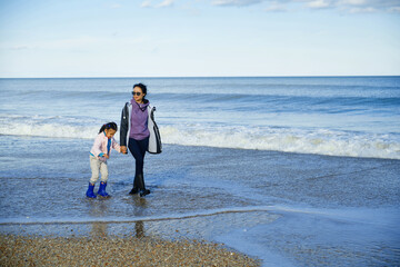 Woman and her daughter walking next to the ocean