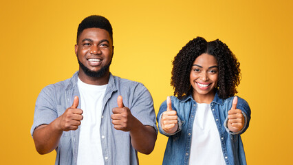 A young man and woman stand side by side, smiling and giving thumbs up. Their casual outfits and...