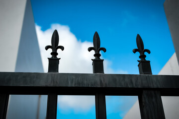 Close-up of fleur de lis finials on a section of black metal fence. elegant architectural or security background isolated against a blue sky © Caroline