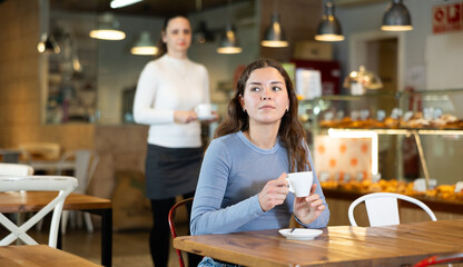 Portrait of young girl with cup in hands drinking coffee in coffee shop indoors