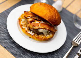 Appetizing cheeseburger with beef patty and fried bacon slices in fluffy bun served on plate. Popular fast food snacks concept..