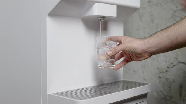 Woman presses a cup of hot water from the water purifier and put it back. Close up look at the glass cup in the kitchen.