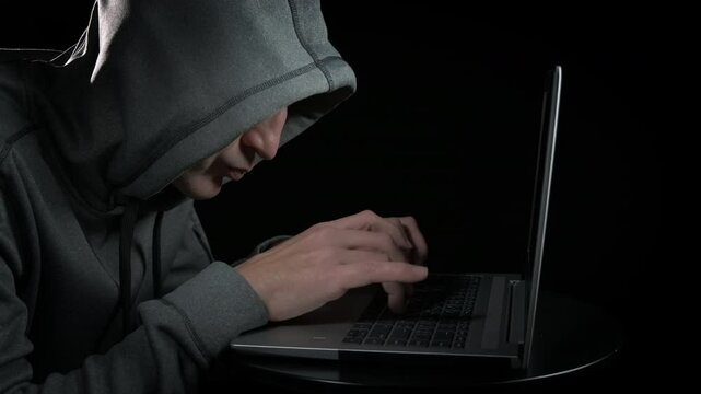Alone thoughtful hacker man with laptop. A view of alone thoughtful man typing on notebook against black background.