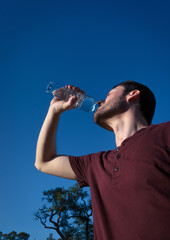 Hombre bebiendo agua en botella al aire libre frente al sol y calor de verano. 