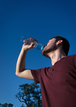 Hombre bebiendo agua en botella al aire libre frente al sol y calor de verano. 