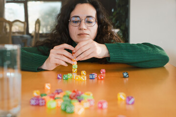 Woman player at her 40s stacking colorful dice during table game night. Female enjoys activity and...