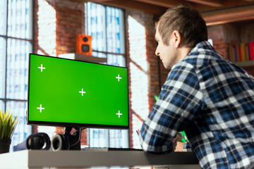 Worker at home office desk browsing internet on mockup PC, researching information online. Man using search engines on green screen computer to find data relevant to work tasks, reading articles