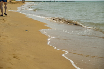 vista dettagliata sul bagnasciuga di una spiaggia, di giorno, in estate, bagnato dall'acqua del mare Adriatico, con le gambe di una persona che cammina sullo sfondo