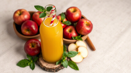 A refreshing bottle of golden apple juice with a striped straw and fresh mint leaves as garnish, placed on a rustic wooden coaster. Surrounding the bottle, organic broth. 