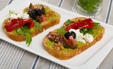 Slices of bread with guacamole and soft cheese decorated with fresh vegetables, herbs and walnut.