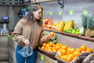 Positive young girl choosing tangerines standing at counter in large fruit and vegetable market