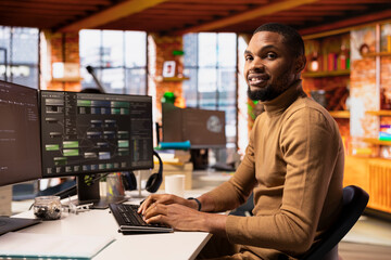 Portrait of smiling IT expert using PC in startup office to design and implementing algorithms...