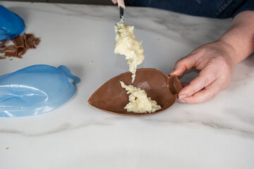 Confectioner putting coconut candy filling in a milk chocolate Easter egg.