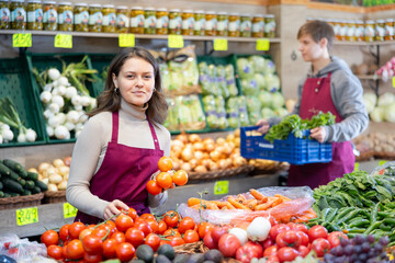 Kind young shop assistant setting tomatoes in vegetable basket in big greengrocery