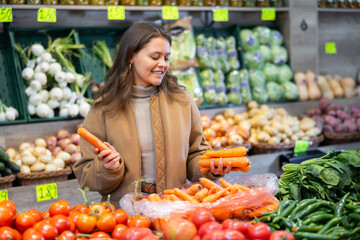 Girl purchaser choosing carrots at the counter in large grocery store
