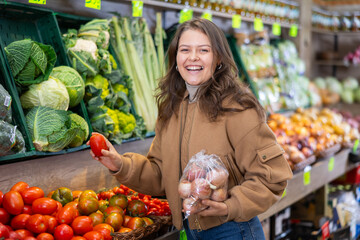 Obraz premium Young woman in casual clothes buys tomatoes in greengrocer's shop..