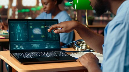 Black med school scholar studying and taking notes using online information, reviews a thesis project in the library. Young man collecting academic data for medical research. Camera B.