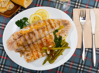 Top view of grilled perch with vegetable garnish of marinated asparagus, greens and lemon on white plate..