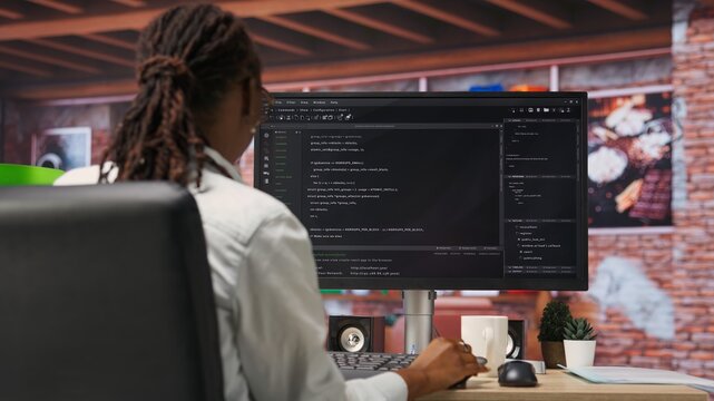 Programmer types code into PC, entering commands, running script. African american IT professional in apartment fixing errors in application, implementing new features, camera B