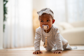 Cute african baby with pacifier crawling on floor, innocent childhood at home, sweet infant...