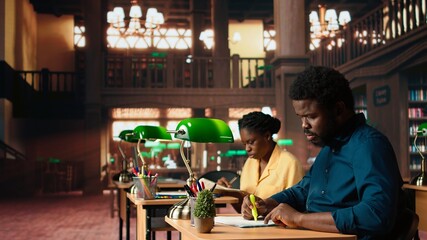 African american pupil underlining key words and phrases at the library, creating a summary with...