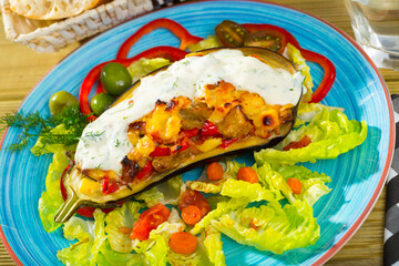 Appetizing eggplant stuffed with stewed vegetables and baked cheese in white sauce on plate