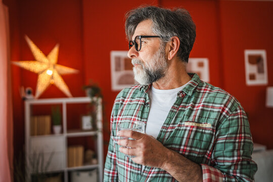 Portrait of mature bearded man stand with glass of water smile at home