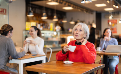 Portrait of mature woman with cup in hands drinking coffee in coffee shop indoors