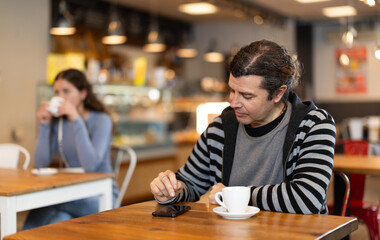 Lonely man drinking coffee and looking at mobile phone screen. Waiting for meeting