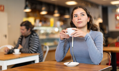 Cafe visitor drinks coffee alone. Girl whiles away time and waits for meeting in chain cafe, spend time while drinking coffee.