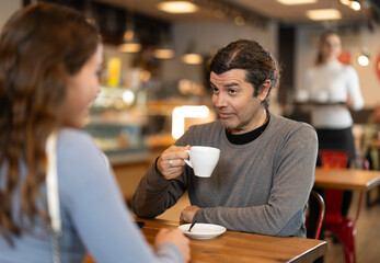 During lunch break, man at cafe drinking coffee, talks with girl, spends time in company of friend. Meeting on neutral territory, discussing personal and business issues