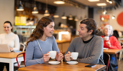 Girl in cafe sits opposite male colleague in cafe, they chat and joke, drinking coffee, spend time. Date, romantic meeting, nice time together. Atmosphere of cafe, restaurant conducive communication