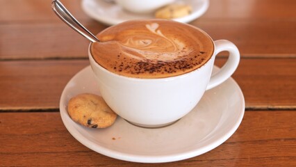 Relaxed cafe atmosphere with steaming cappuccino and soft lighting Velvety foam rich coffee flavor and rustic wooden table create perfect setting for quiet break Concept of theme drinkingf coffee