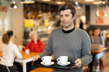 Breakfast in cafe - man carries tray with two cups of coffee