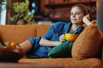 Happy woman sitting on a couch with a cup of coffee in hand, smiling pleasantly
