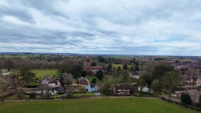 Aerial drone shot of Holy Trinity Church of England Church in Eccleshall, Staffordshire, UK on a spring afternoon. It is overcast. We see beautiful english countryside in the distance. 