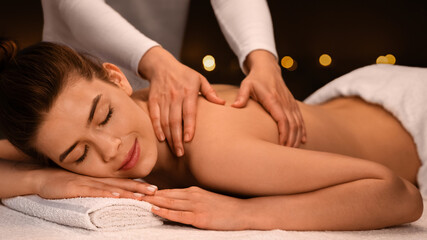 Massage therapist hands rubbing girl shoulders at modern spa, side view