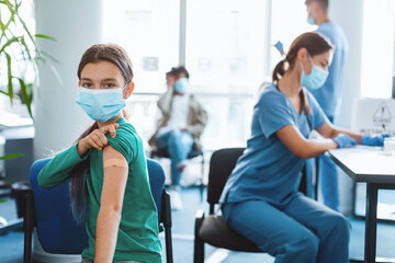 Obraz premium Children and a nurse participate in a vaccination campaign at a clinic. A young girl smiles with a bandage on her arm after receiving the flu shot, promoting health awareness.