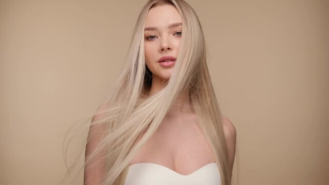 Beautiful woman with blond healthy hair on beige background. Hair beauty.