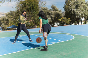 Obraz premium Young women playing basketball, one with prosthetic leg dribbling ball on outdoor court