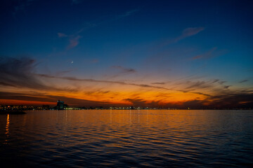 Obraz premium Tranquil Twilight Over the Arabian Gulf with a Crescent Moon and Vibrant Sunset Reflections in Kuwait