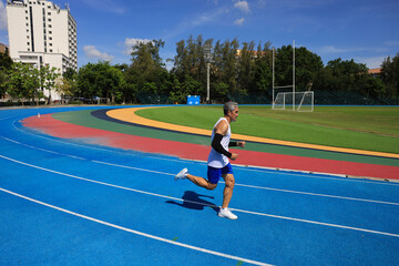 Senior Asian athlete is practicing running in the professional blue track for professional exercise, sport training workout and healthy for longevity concept