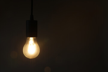 Glowing light bulb hanging on dark background. Space for text