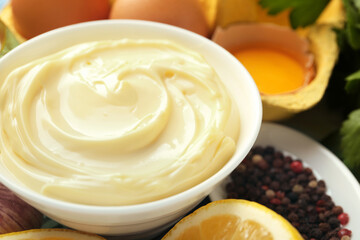 Delicious mayonnaise sauce in bowl and ingredients on table, closeup